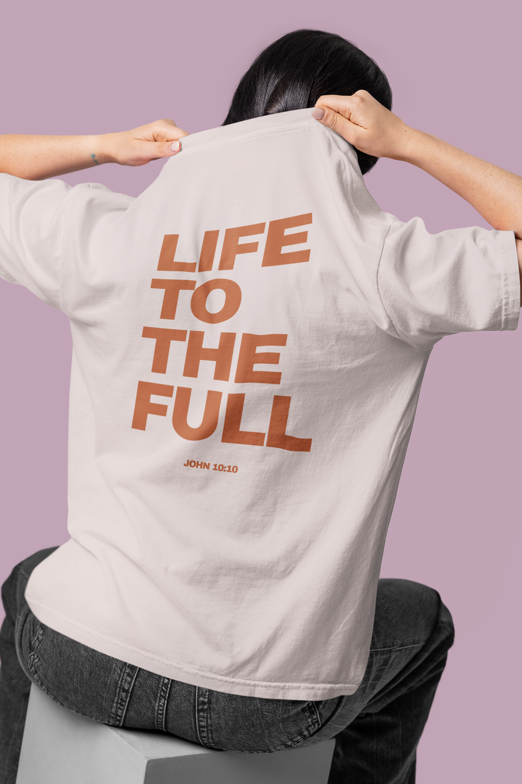Person wearing a shirt with 'Life to the Full' text on the back against a purple background