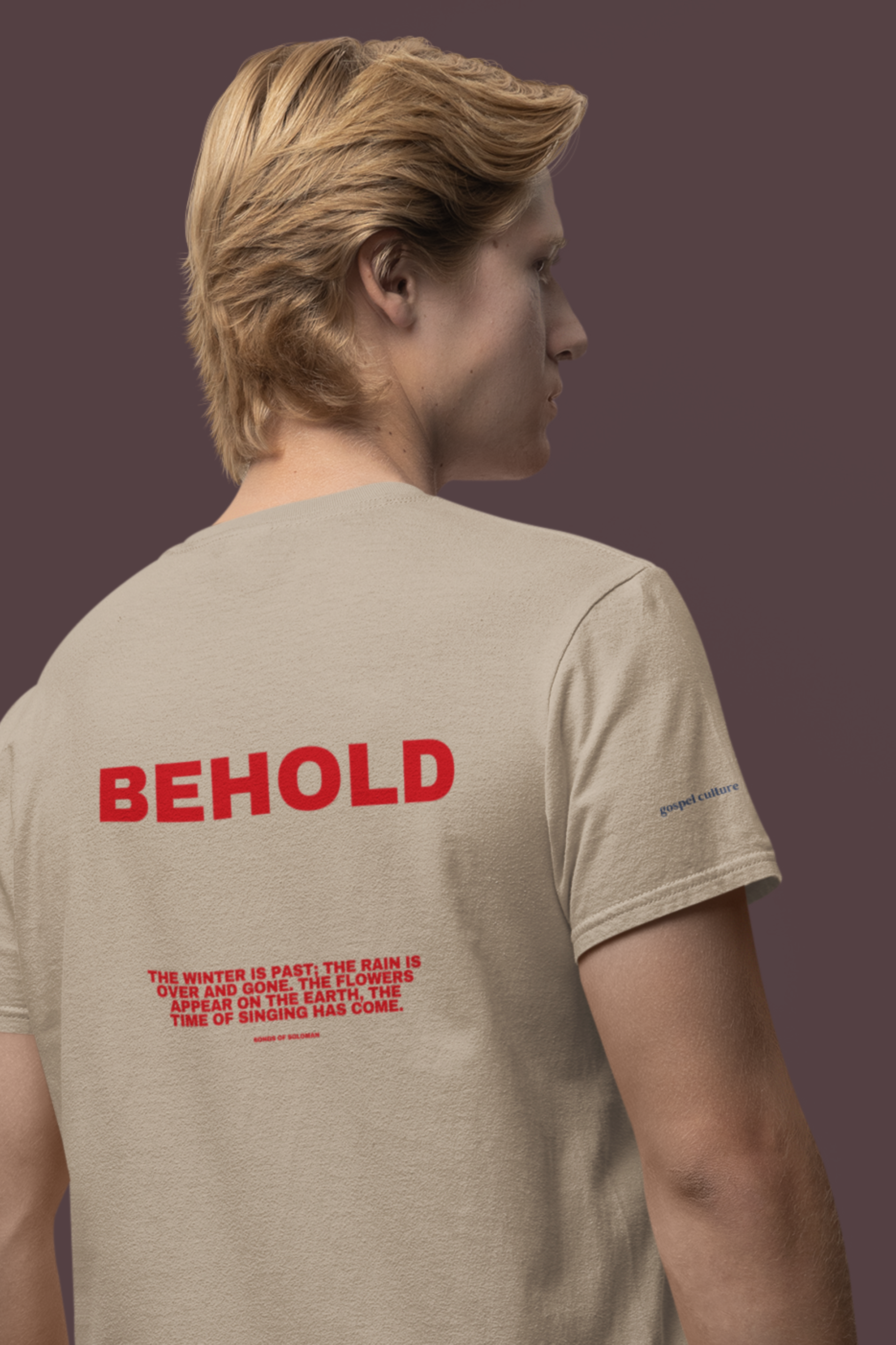 Person wearing a beige t-shirt with red text on the back against a brown background