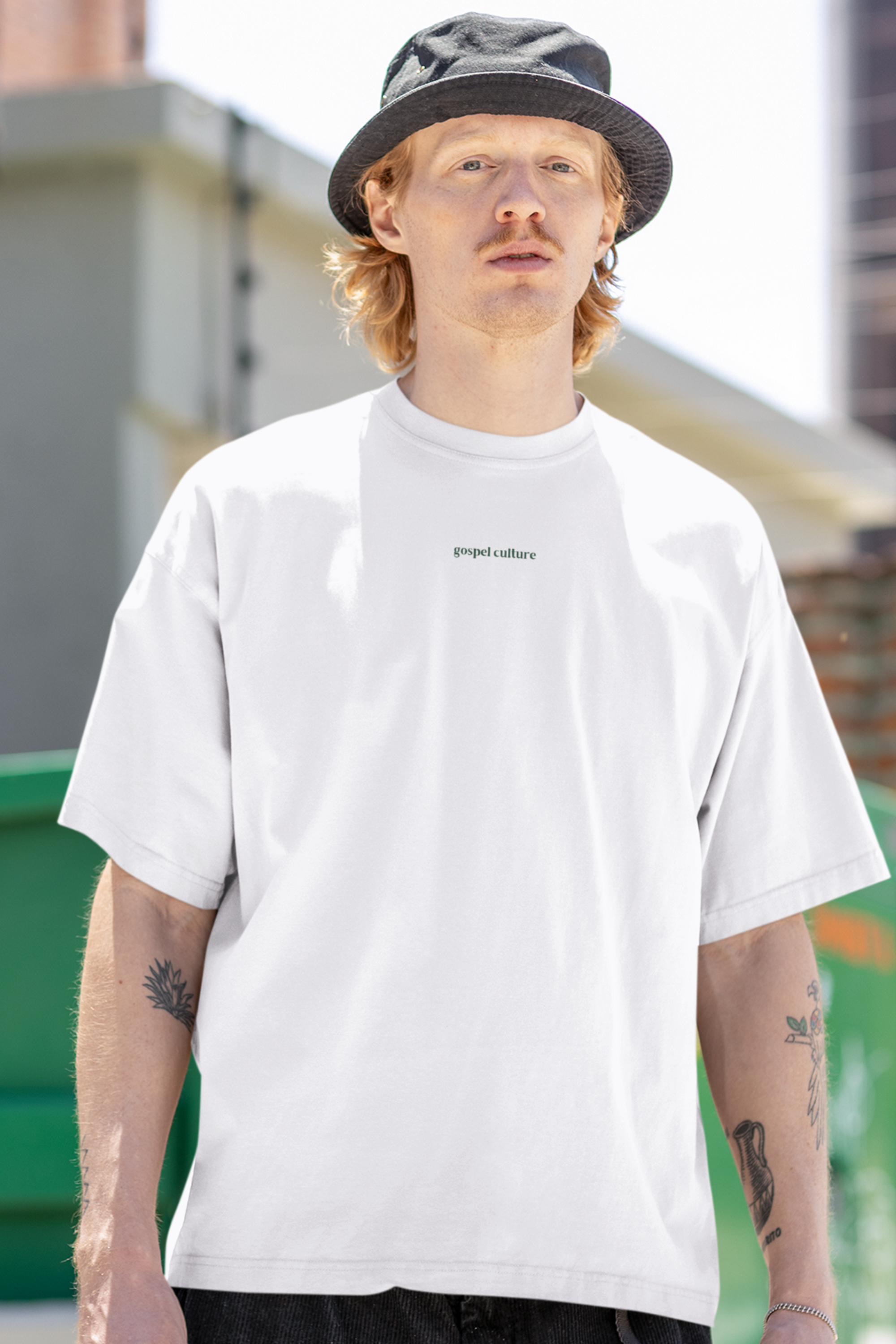 Person wearing a white t-shirt with gospel culture logo and a hat, standing outdoors.