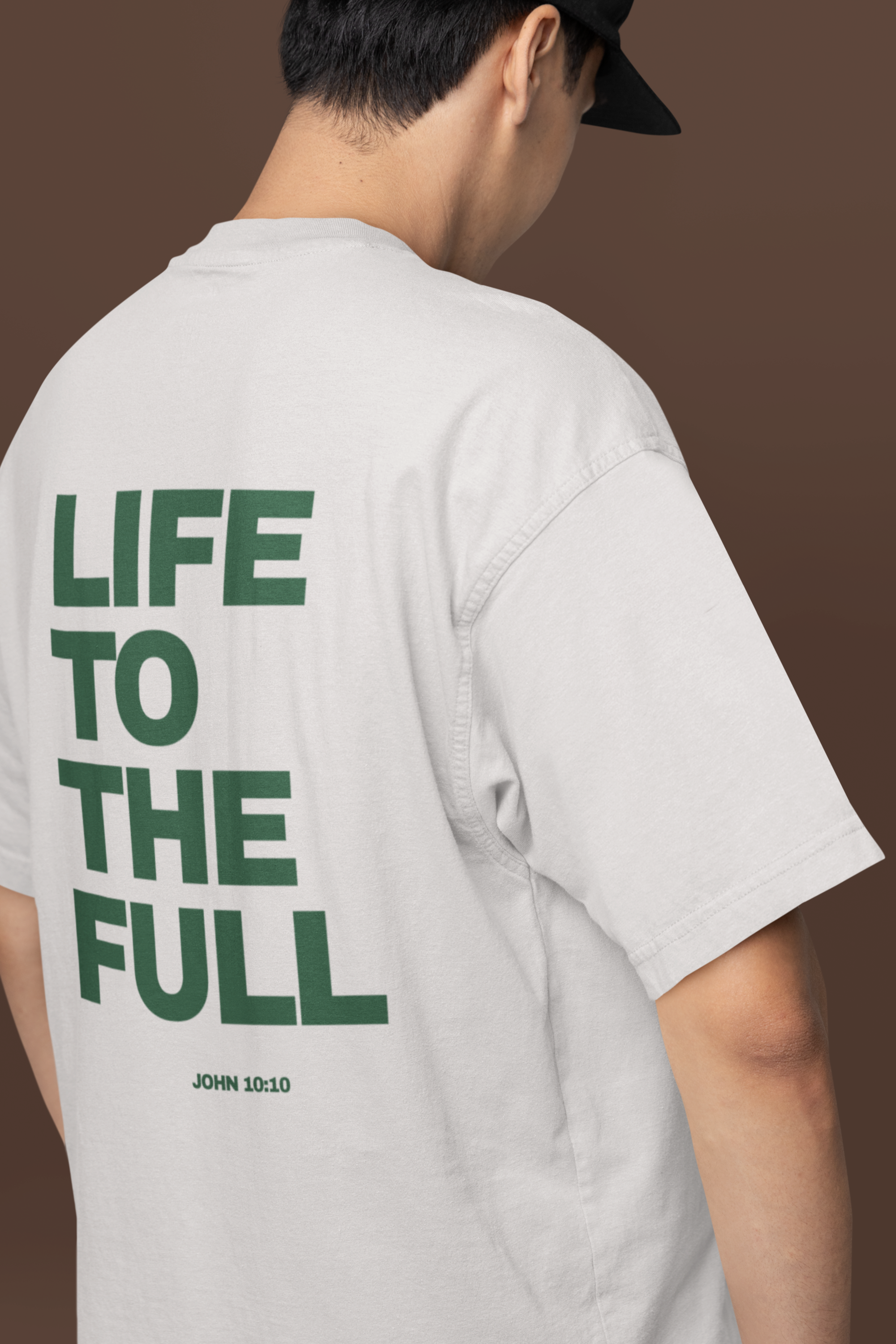 Person wearing a white t-shirt with 'LIFE TO THE FULL' text on the back against a brown background