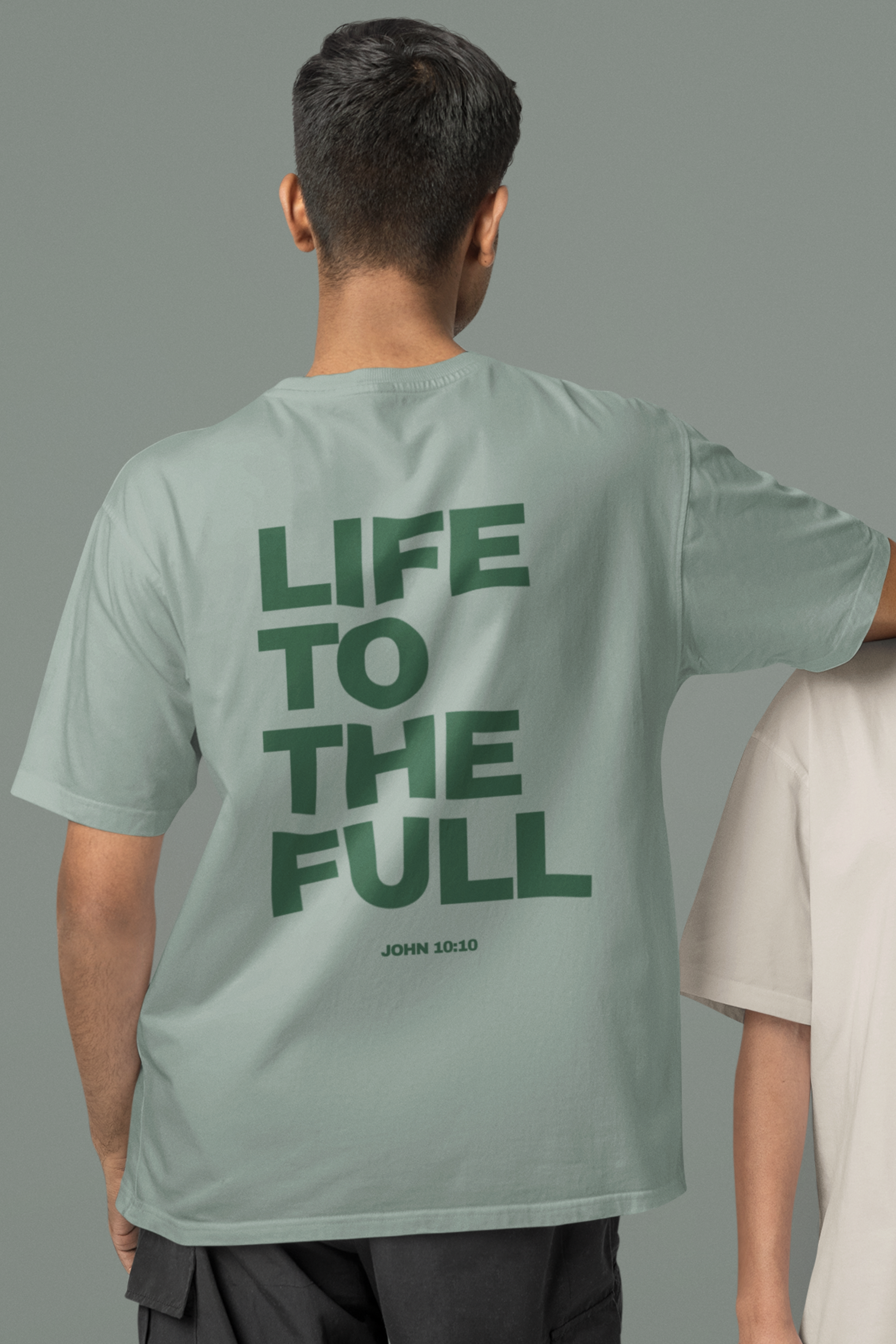 Person wearing a light green t-shirt with 'LIFE TO THE FULL' text on the back, standing against a gray background.