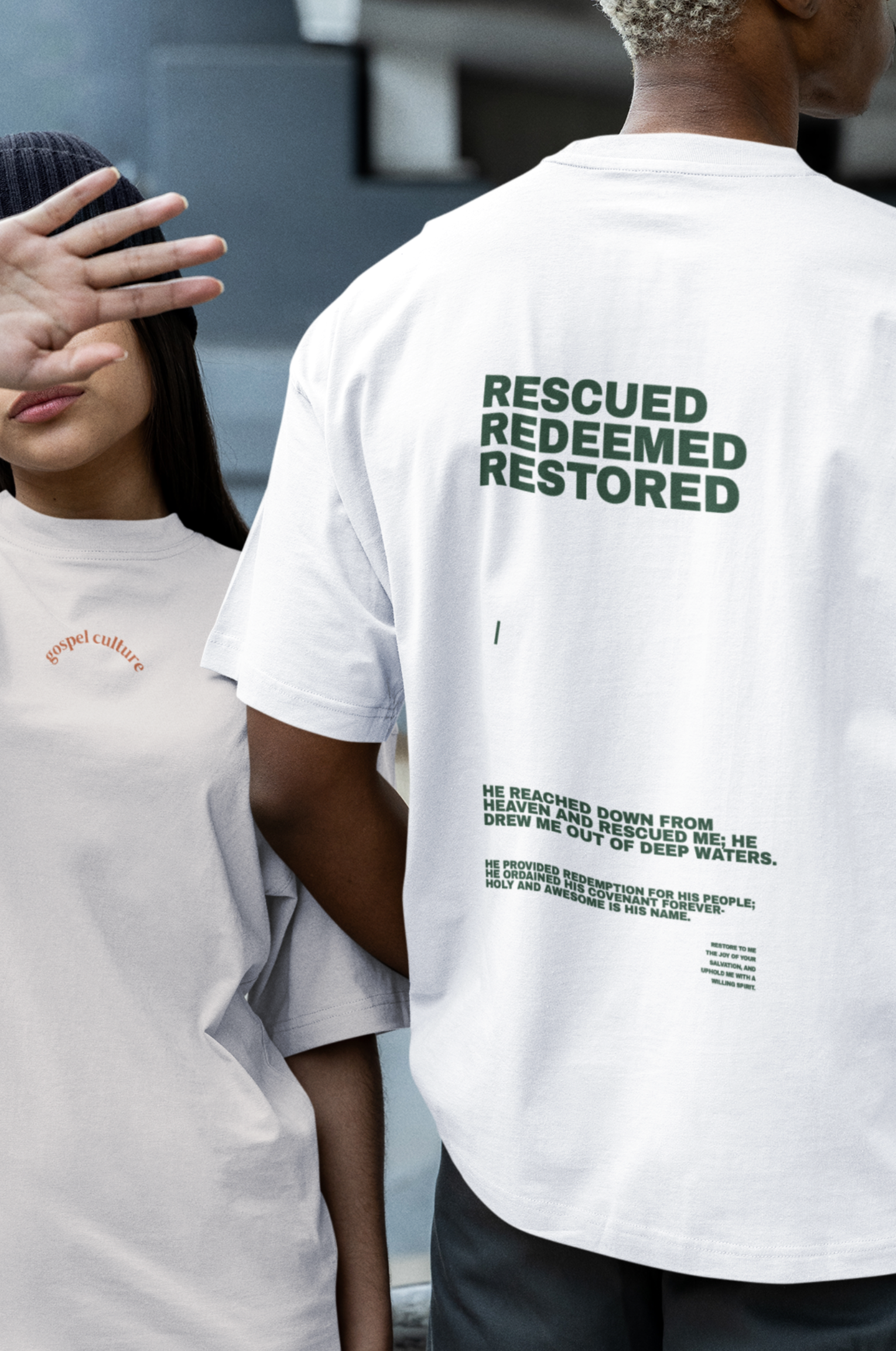 Two people wearing white t-shirts with text, standing on a street.