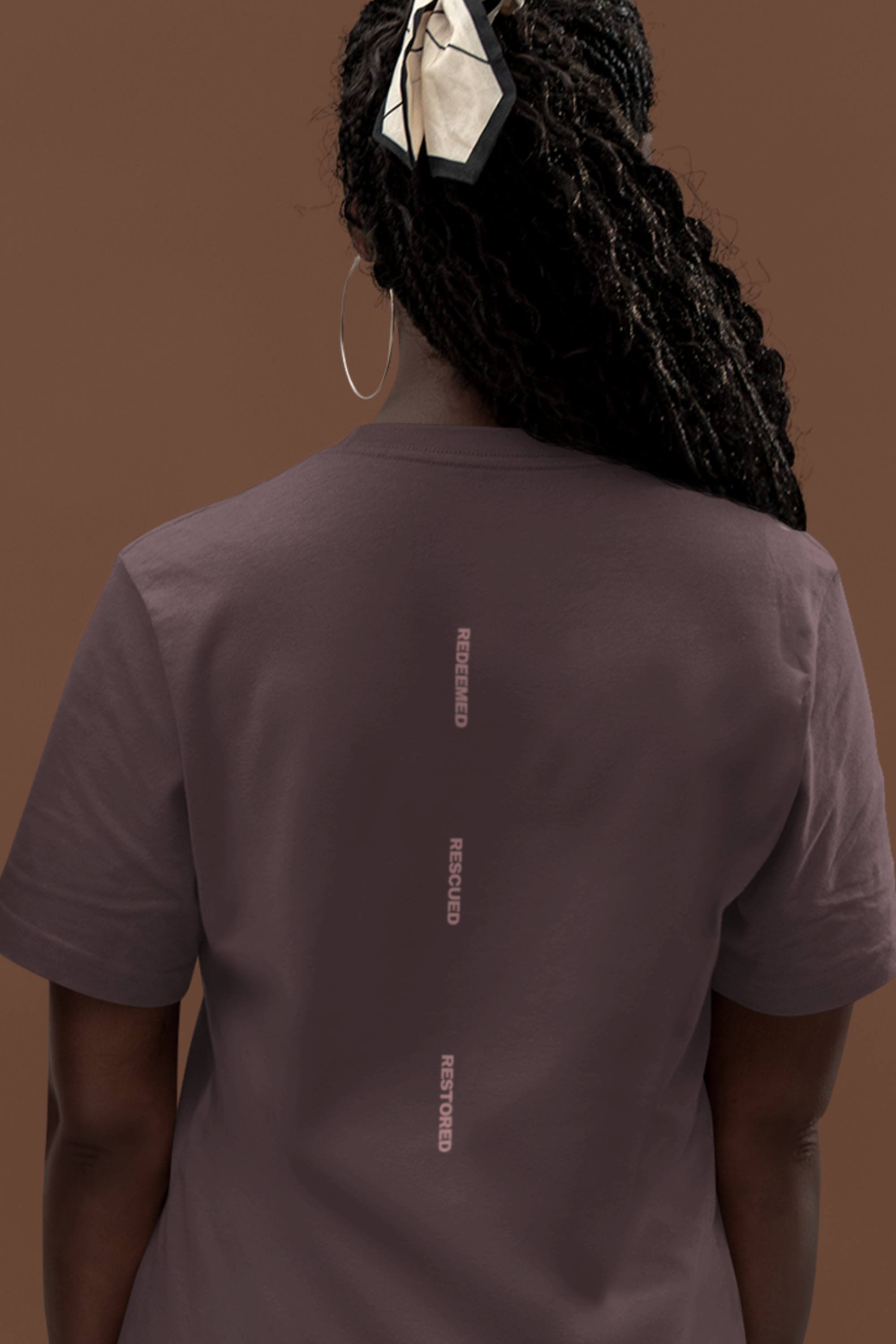 Person wearing a brown organic cotton christian t-shirt with text on the back against a brown background