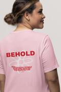 Woman wearing a pink t-shirt with 'BEHOLD' text on the back, against a plain background